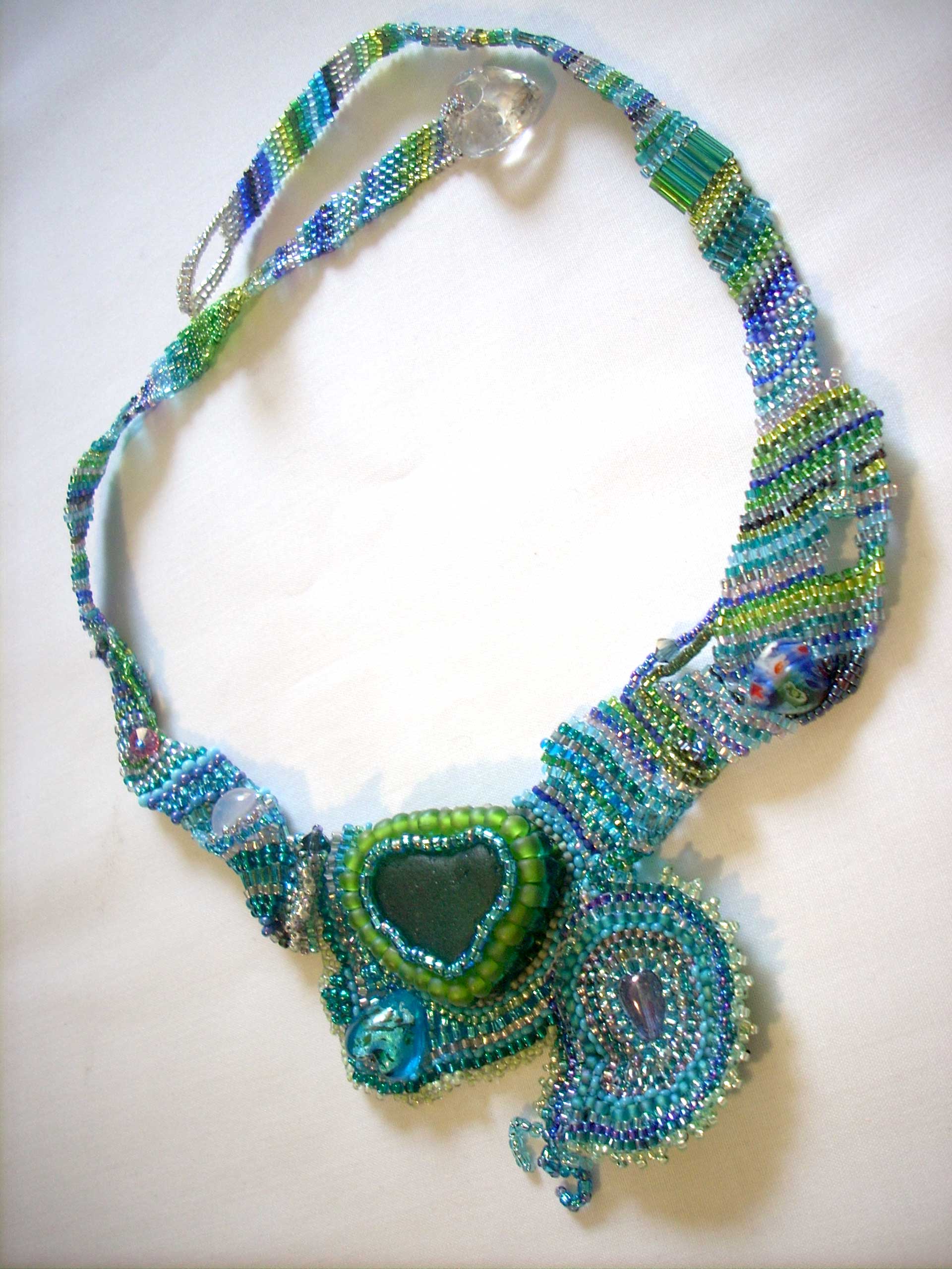 baroque handmade necklace with deep green heart of sea glass surrounded by seed beads in greens and blues